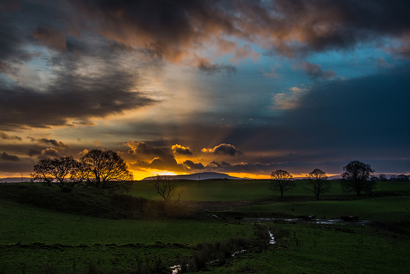 dramatic sunrise with clouds sunbeams and pastoral setting