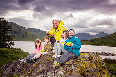 Tim and kids sitting on a rock eating hills and loch Arklet behind