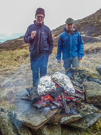 two men in front of a small cooking fire on a windy day